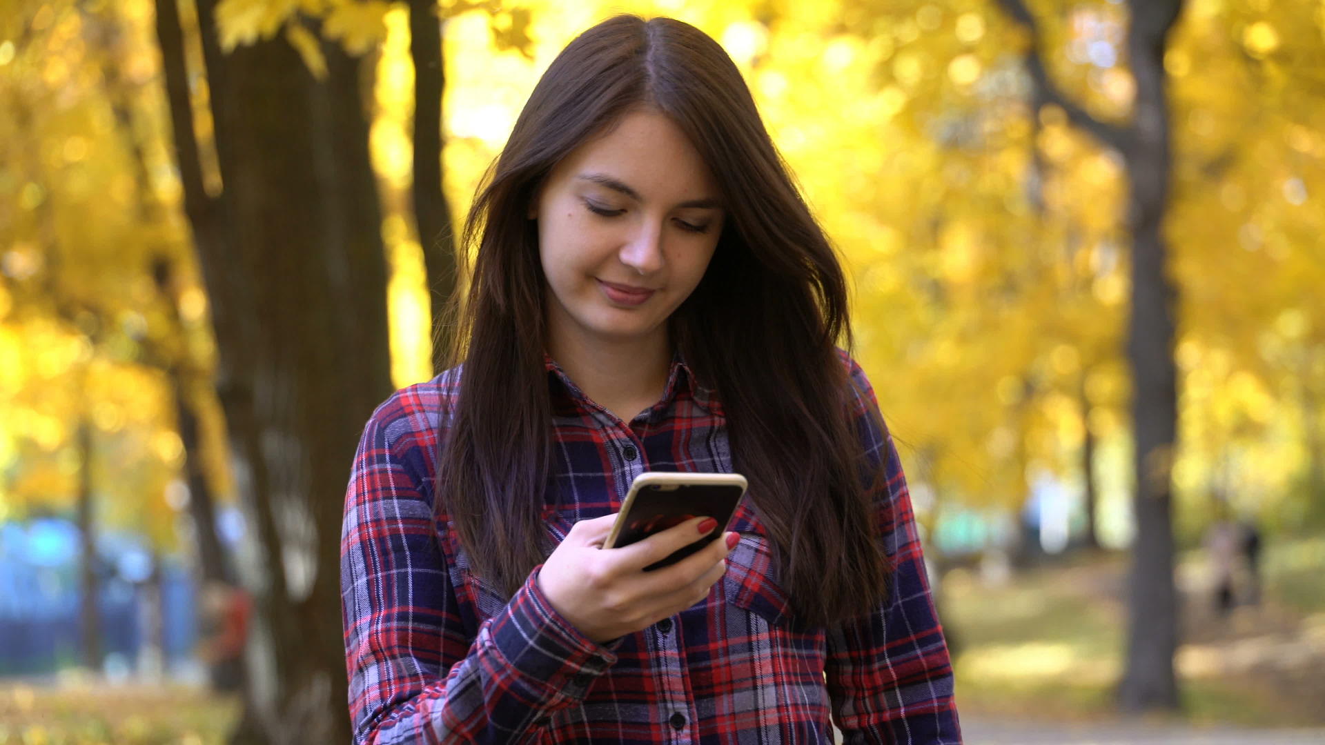 秋天女孩在公园里散步在她的智能手机上使用应用视频视频的预览图