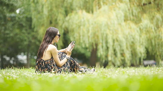 可爱的女人坐在公园里看手机短信视频的预览图