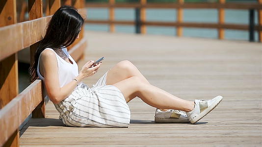 可爱的女人坐在公园里看手机短信视频的预览图