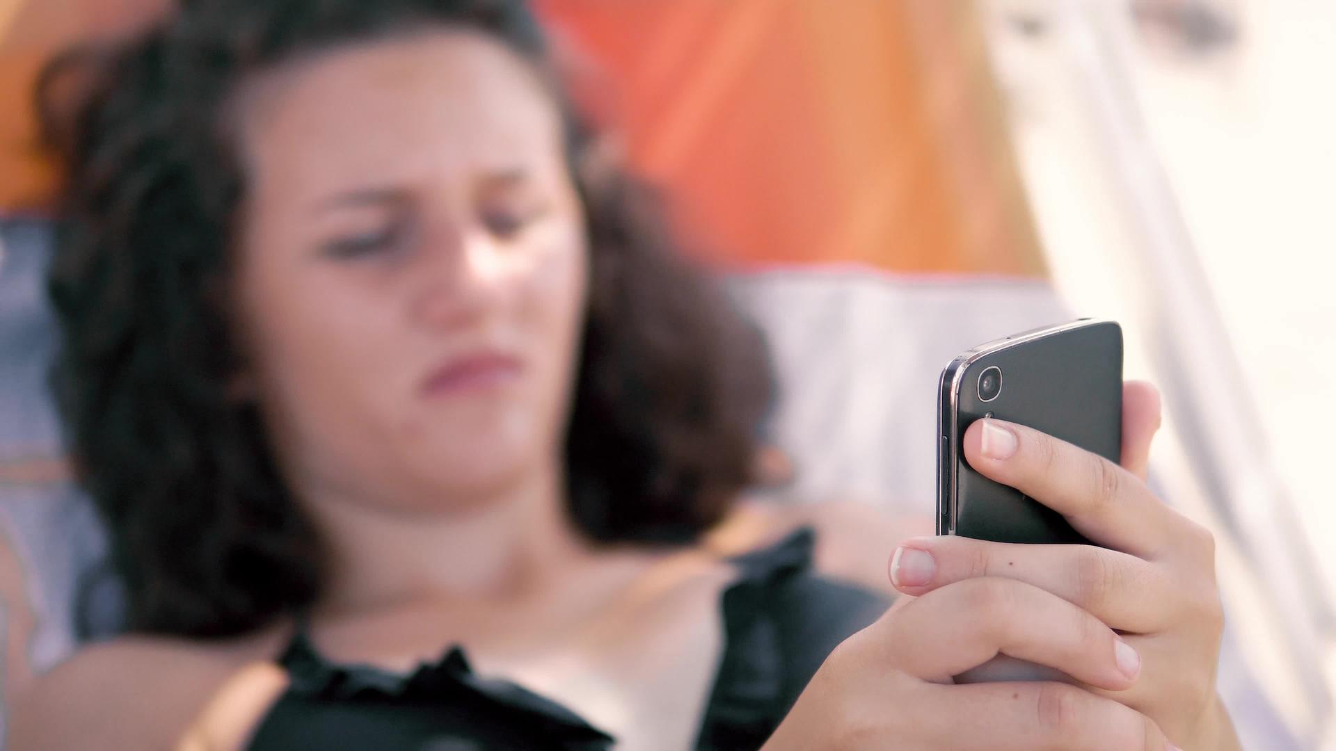 女青少年用手指在沙滩上的智能手机上打字Dof视频的预览图