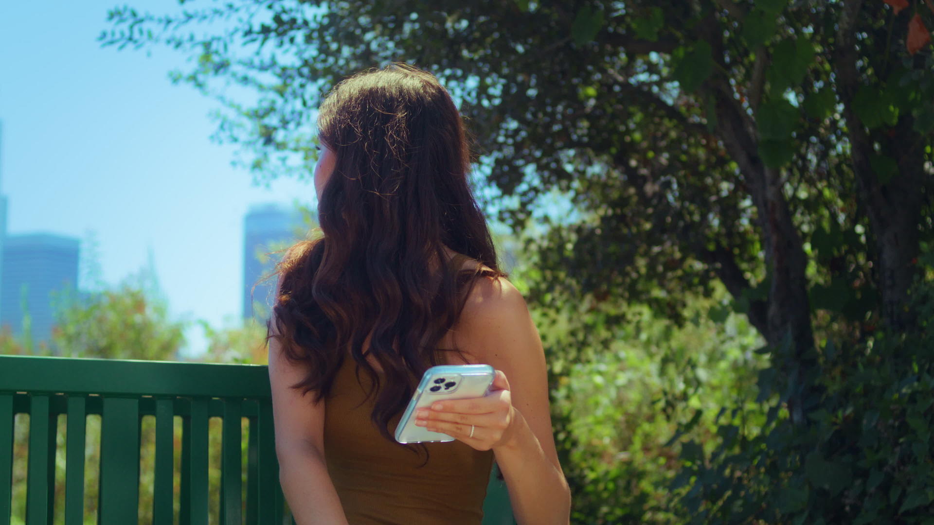 在公园特写镜头中亚洲妇女手持智能手机回顾模糊的城市景观视频的预览图