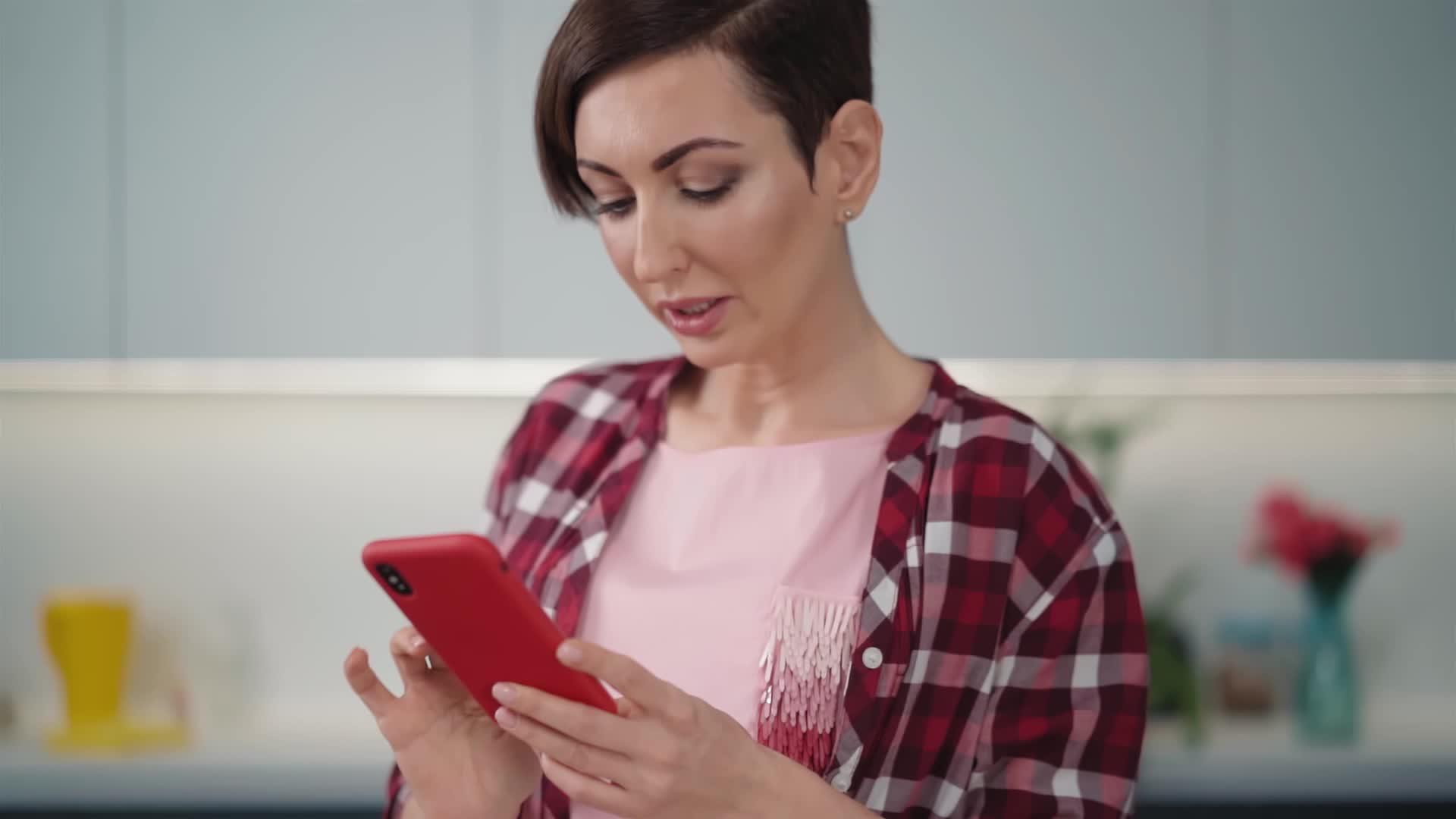 用她的红色智能手机在现代明亮厨房做饭视频的预览图