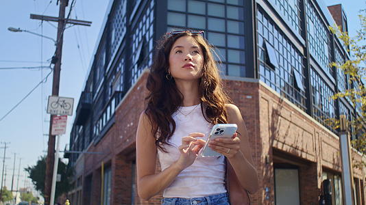 年轻女子用智能手机站在十字路口视频的预览图