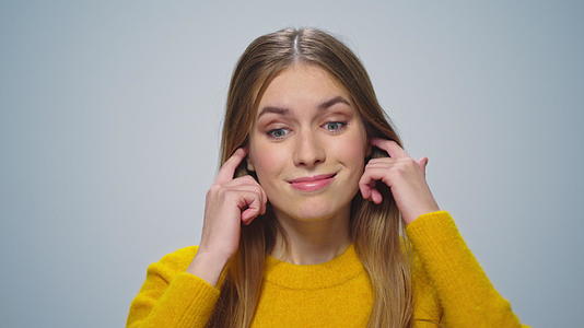 一个微笑的女人的肖像用手指在摄影棚的镜头上遮住了她的耳朵视频的预览图
