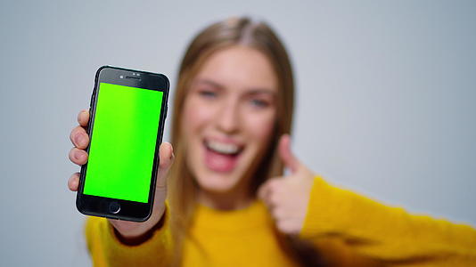 微笑的女性在演播室用绿色屏幕显示智能手机视频的预览图