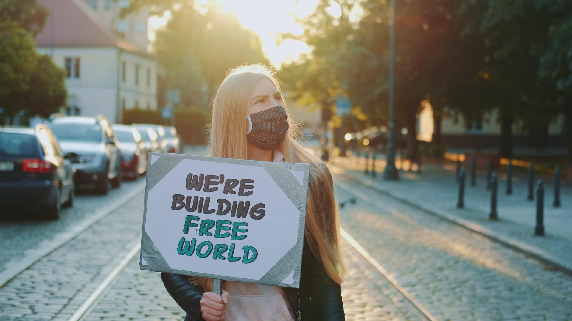 戴着保护口罩的金发女性用口号建立自由世界视频的预览图