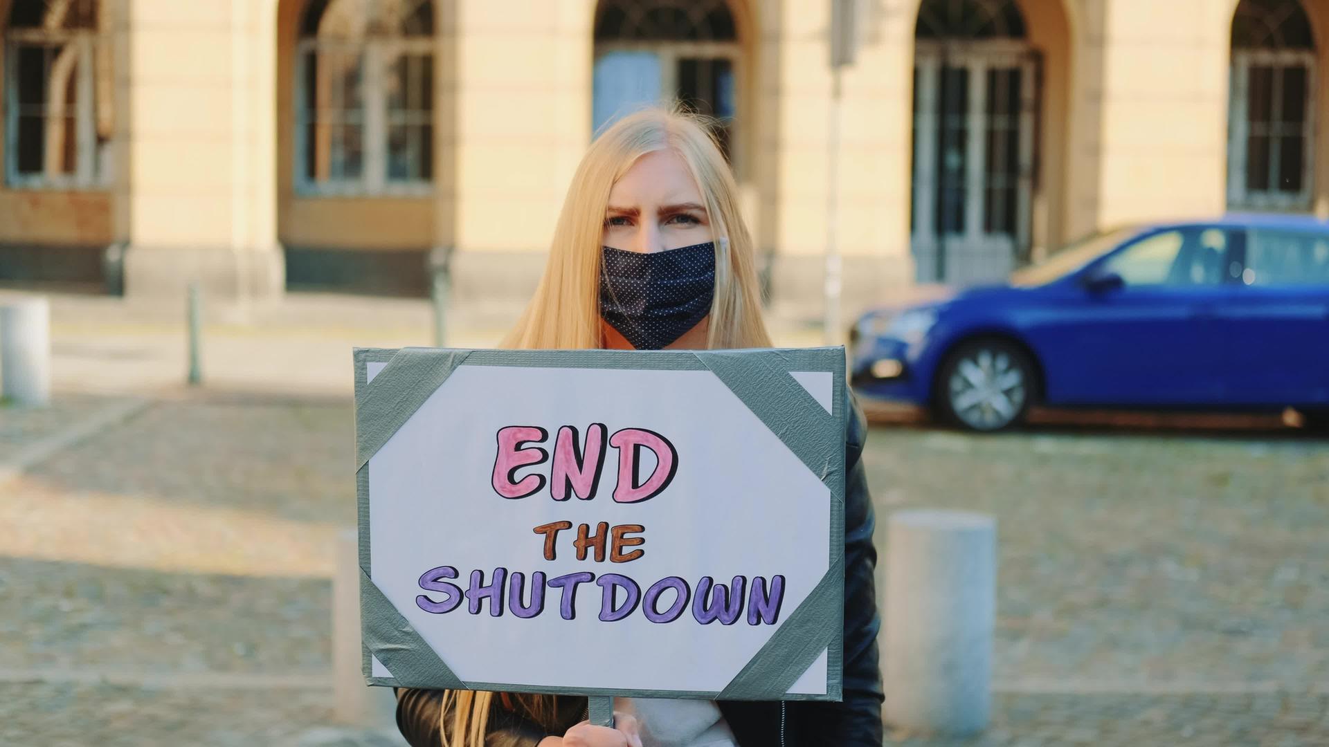 戴着抗议横幅的蒙面妇女呼吁结束关闭视频的预览图