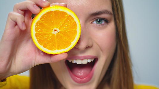 特写年轻美女在室内用两片橙色切割成面孔视频的预览图