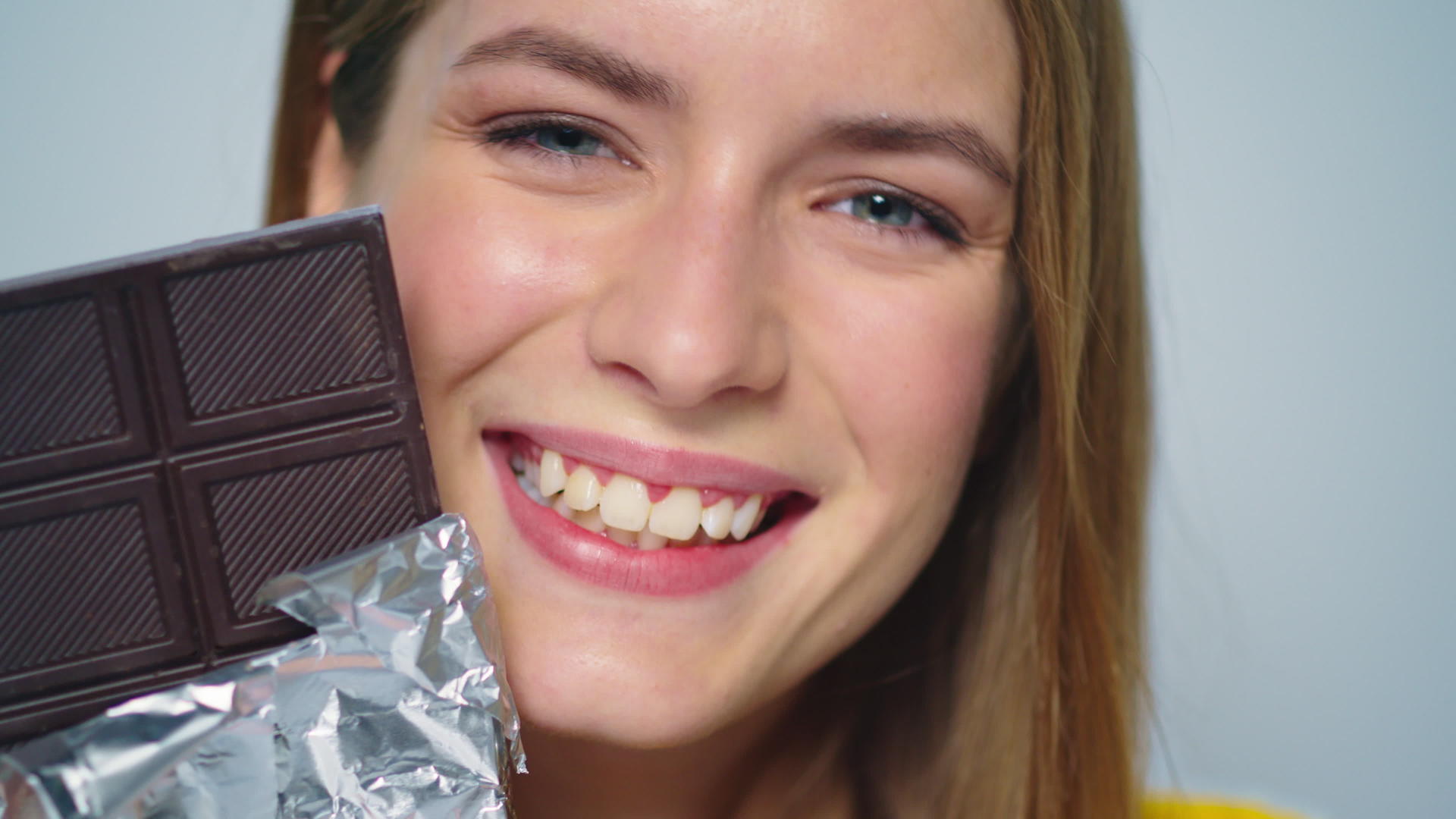 年轻女子看着相机的灰色背景和巧克力条视频的预览图