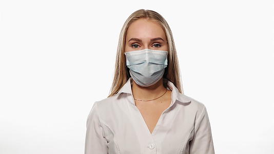 年轻护士用医用面具点头作为协议看着白色背景上的镜头视频的预览图