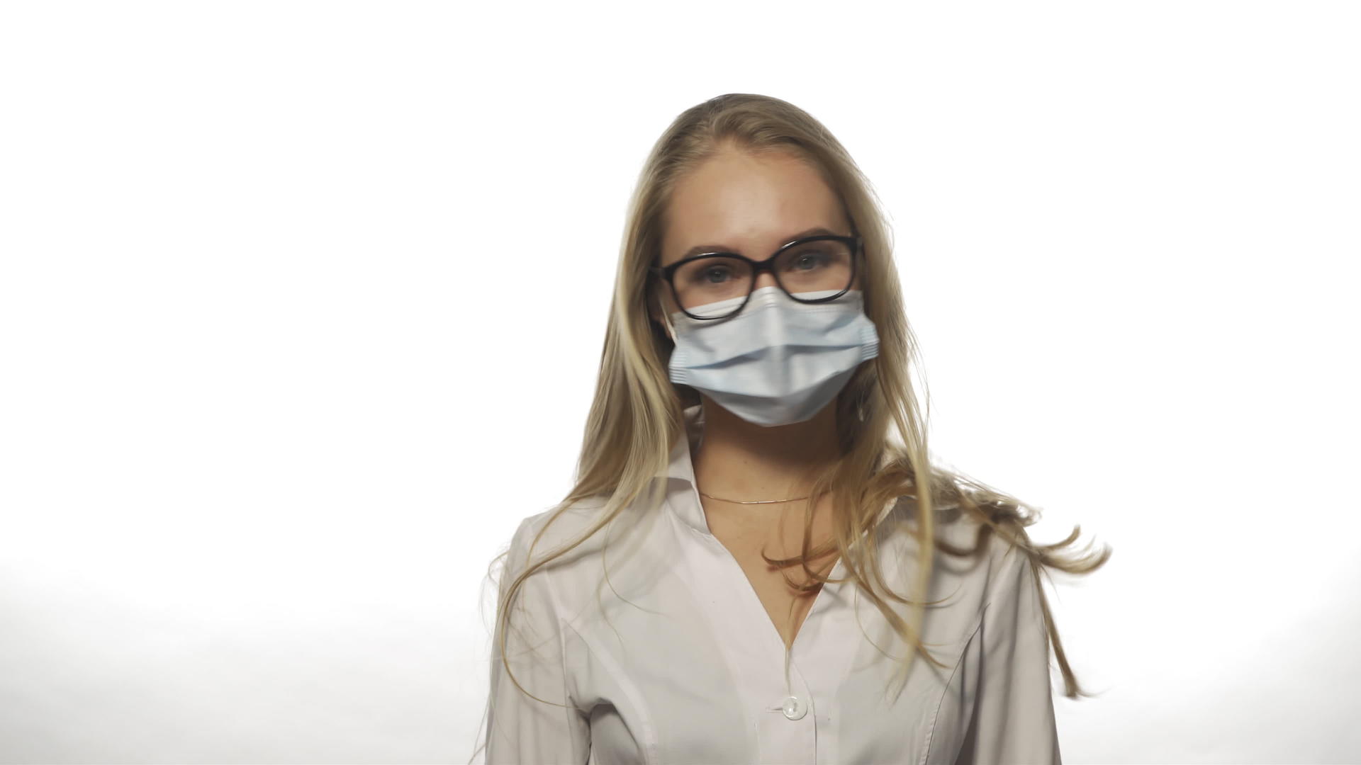 一名身穿长袍的年轻护士摘下一个戴着白色眼镜的医疗面具视频的预览图