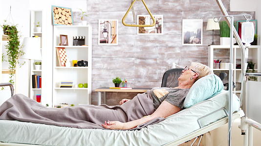 退休残疾妇女躺在医院的床上在养老院舒适明亮的房间里视频的预览图