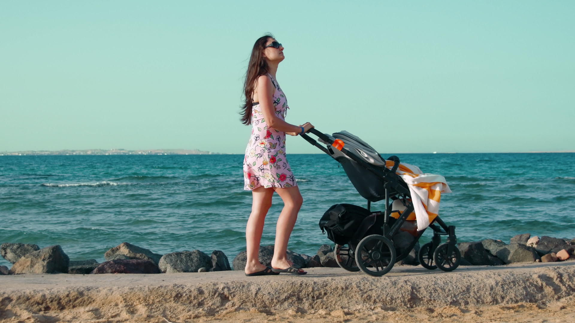 留着长发的年轻母亲推着婴儿车在海边散步视频的预览图