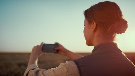 在金色的阳光下女人在麦田里拍照视频的预览图