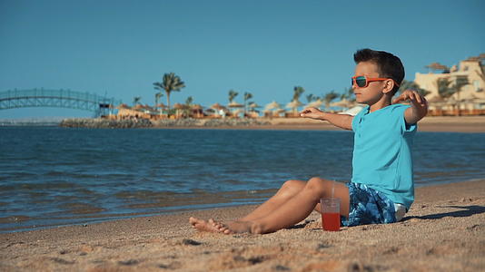 夏天的暑假小男孩坐在沙滩上带着果汁视频的预览图