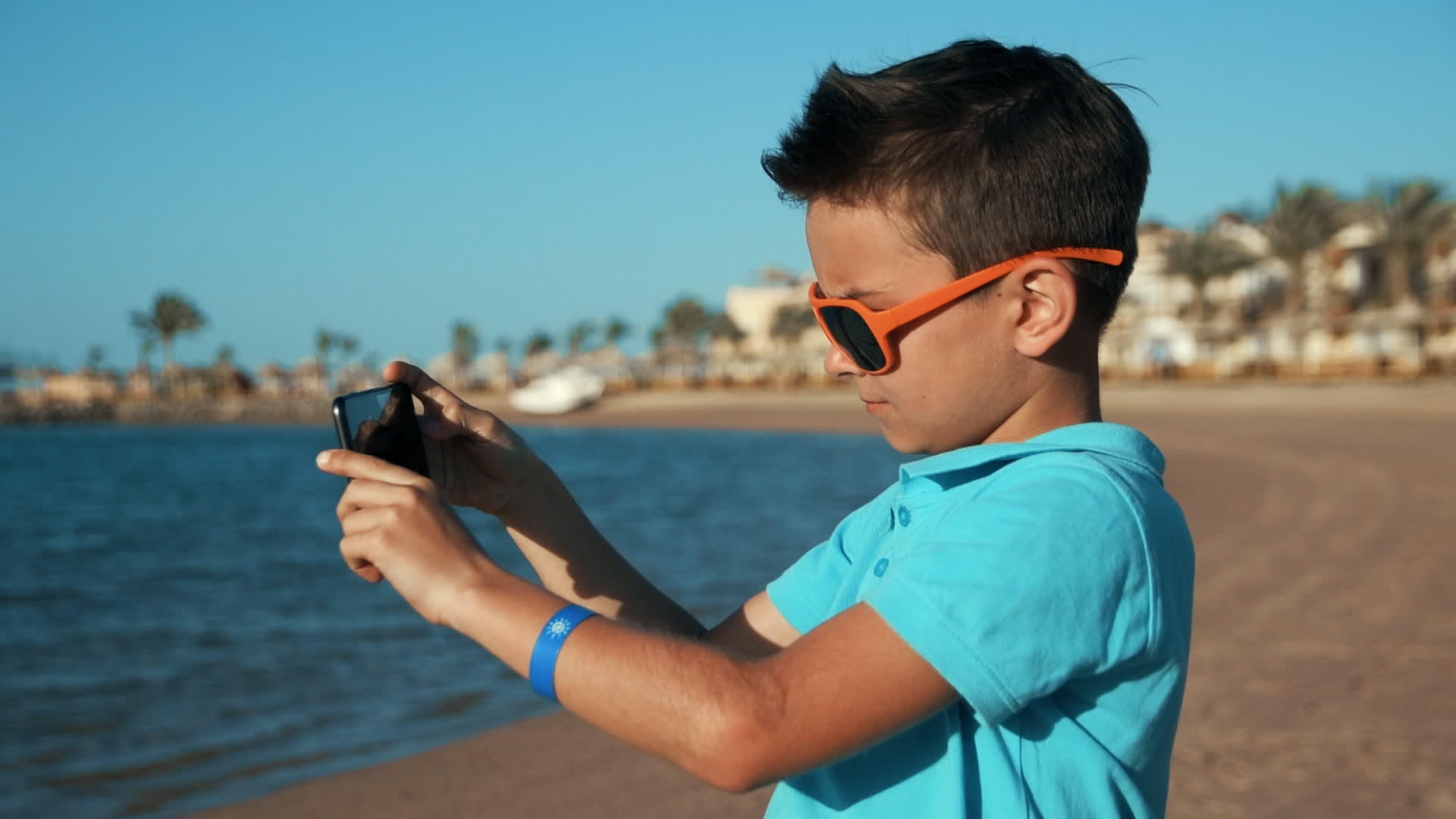 小男孩用手机在阳光明媚的海岸线上拍照视频的预览图