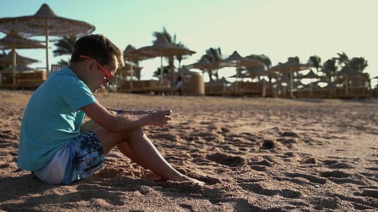 小男孩在海边玩手机游戏视频的预览图