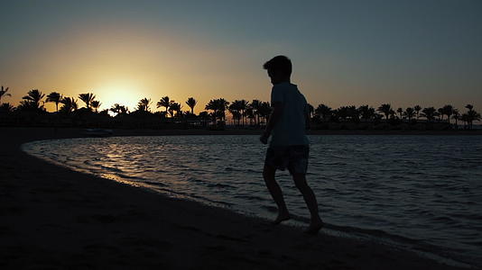 小男孩日落时在海上奔跑视频的预览图