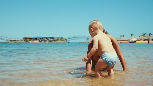 小女孩和弟弟在阳光明媚的海边玩水视频的预览图