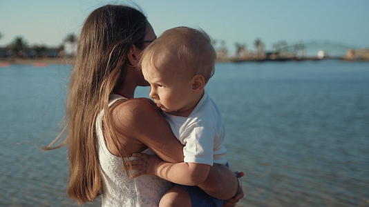 可爱的小女孩抱着她的弟弟在美丽的海岸上享受着阳光明媚的早晨视频的预览图