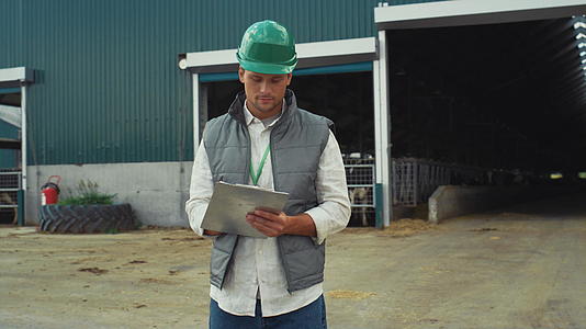 专业工程师戴着防护头盔在现代牛棚建筑中做笔记视频的预览图