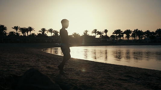 少年男孩在沙滩上行走日落背光剪影视频的预览图