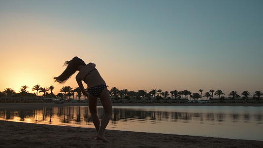 快乐的小女孩在日落的海边快乐地跳舞视频的预览图