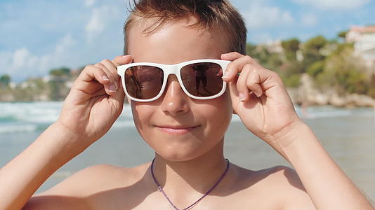 快乐的男孩戴着太阳镜在海边看着镜头享受夏天视频的预览图