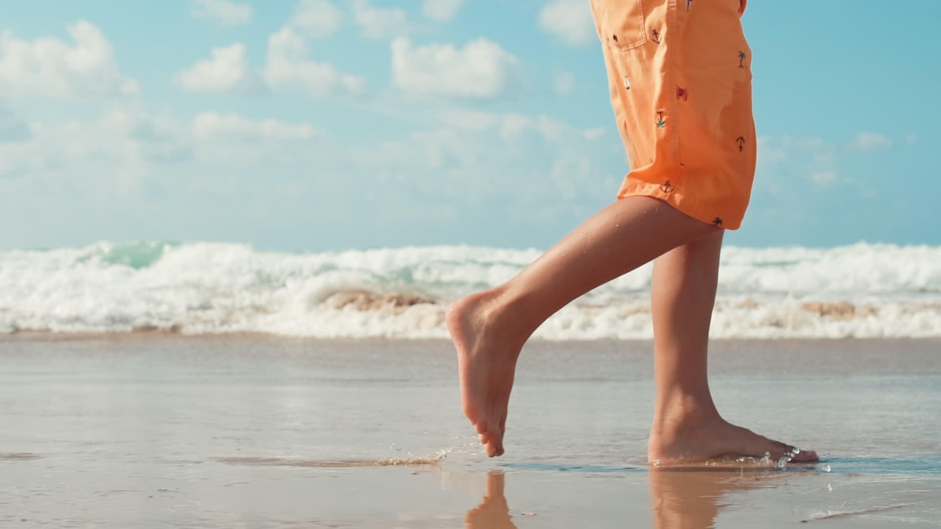 小男孩在海滩上散步留下脚印和腿部特写视频的预览图