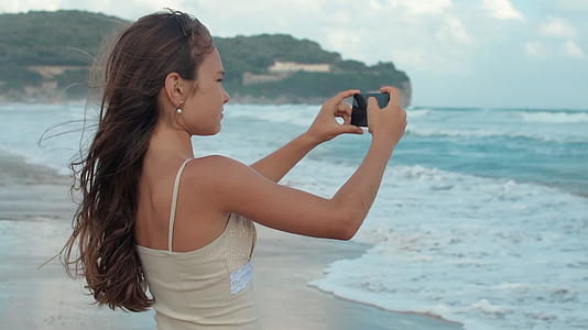 快乐的女孩在海边度过暑假用手机拍照视频的预览图