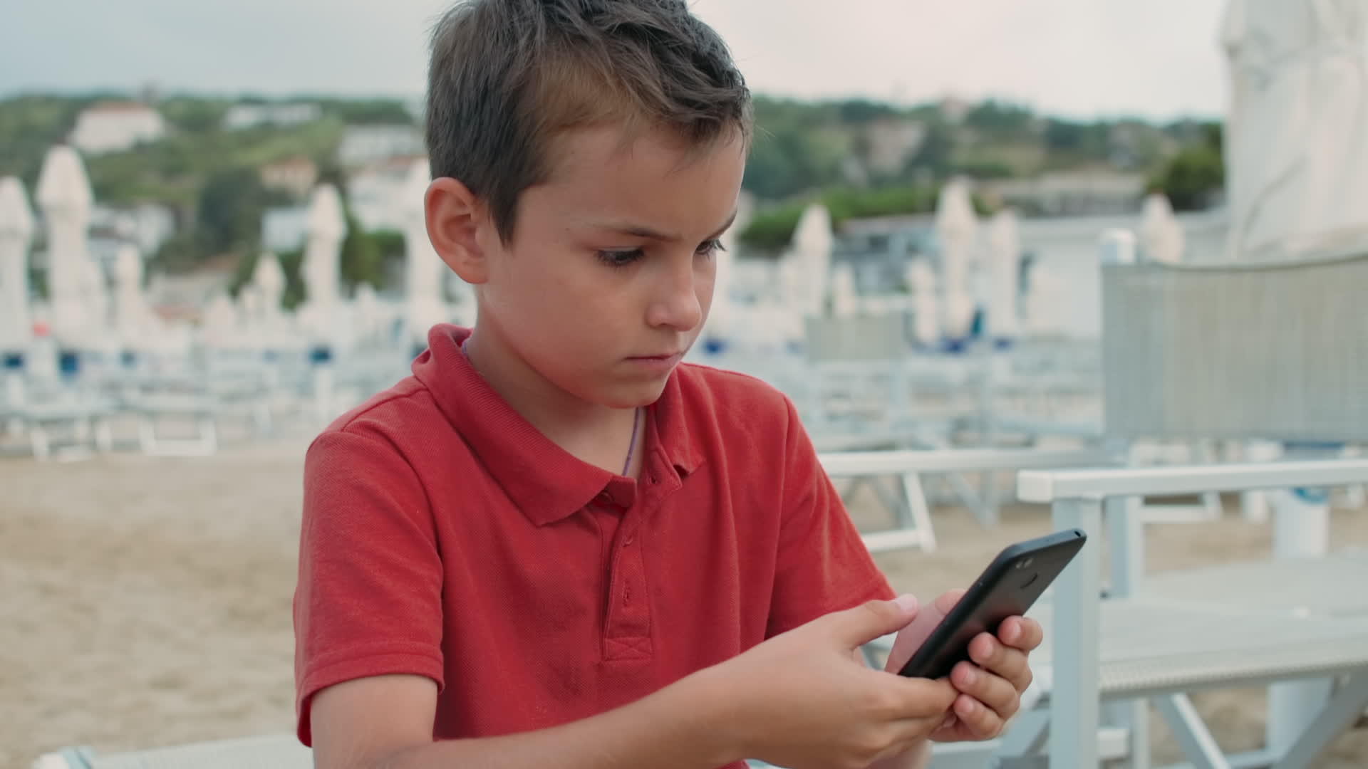 小男孩拿着手机在海滩上看信息视频的预览图