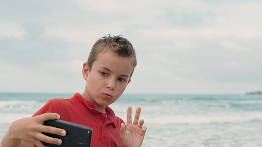 小男孩用手机在海滩上拍照视频的预览图