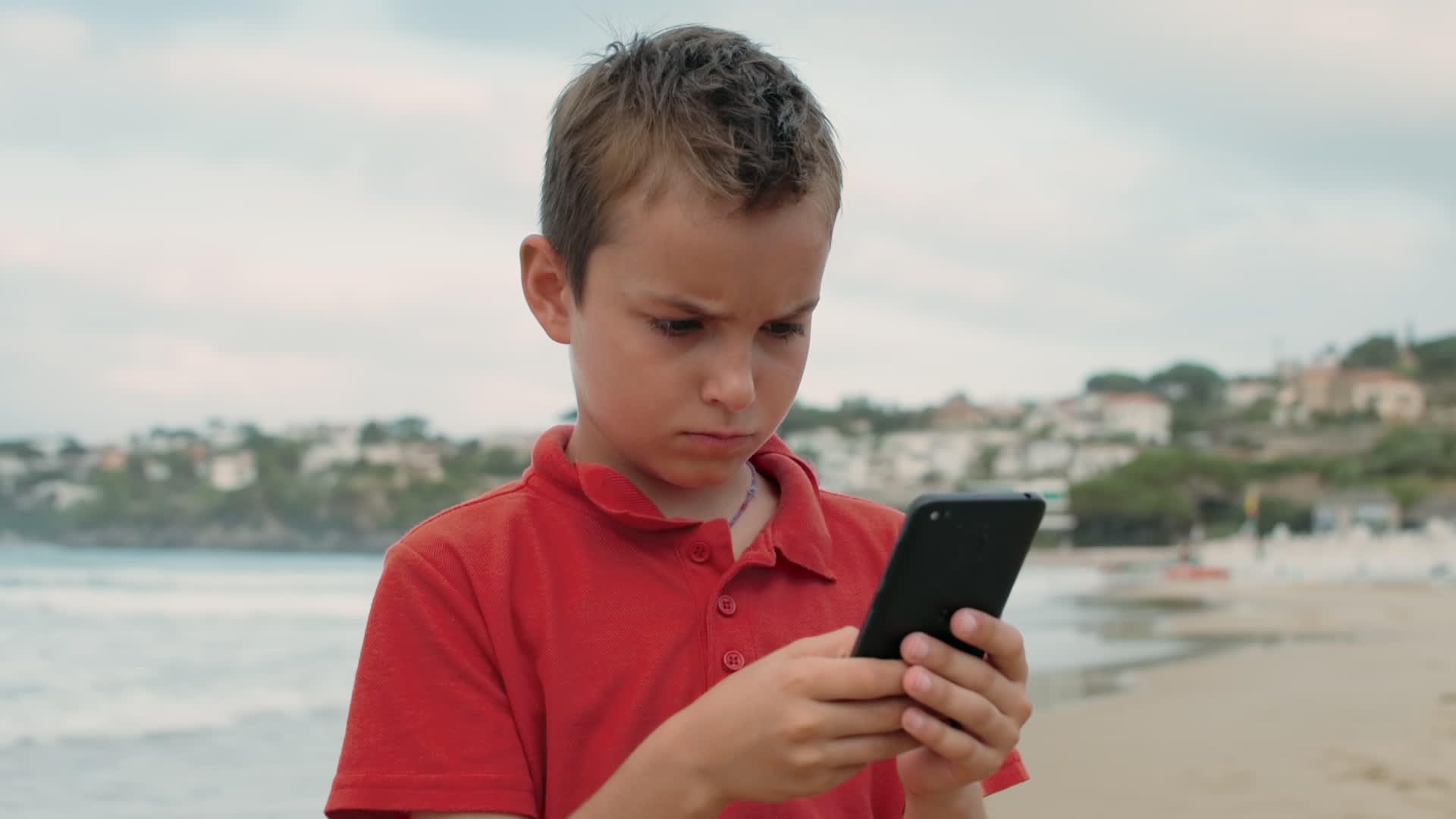 海边的小男孩用手机皱着眉头视频的预览图