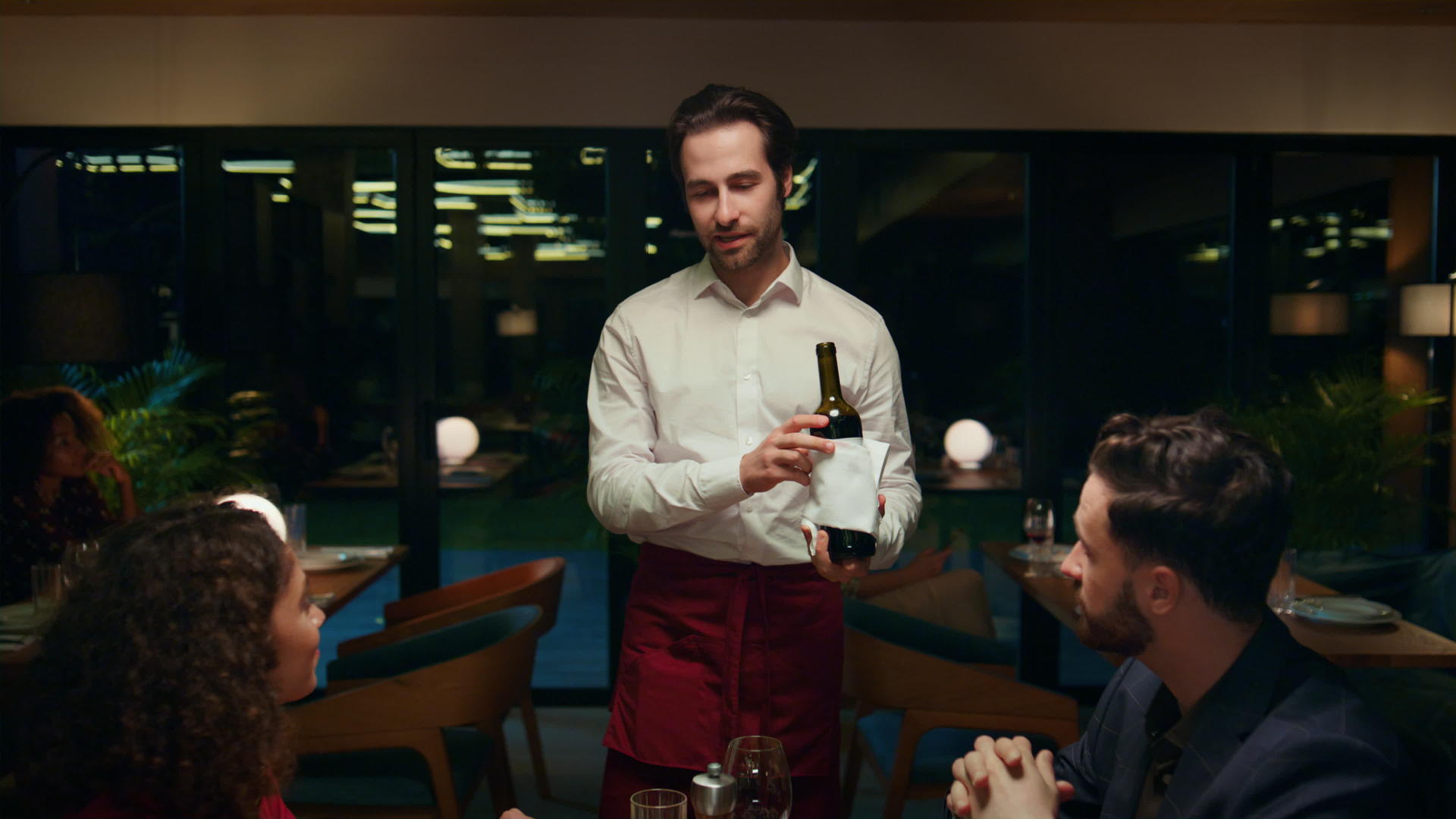 餐厅服务员在花哨的咖啡桌上倒酒为一对美丽的夫妇服务视频的预览图