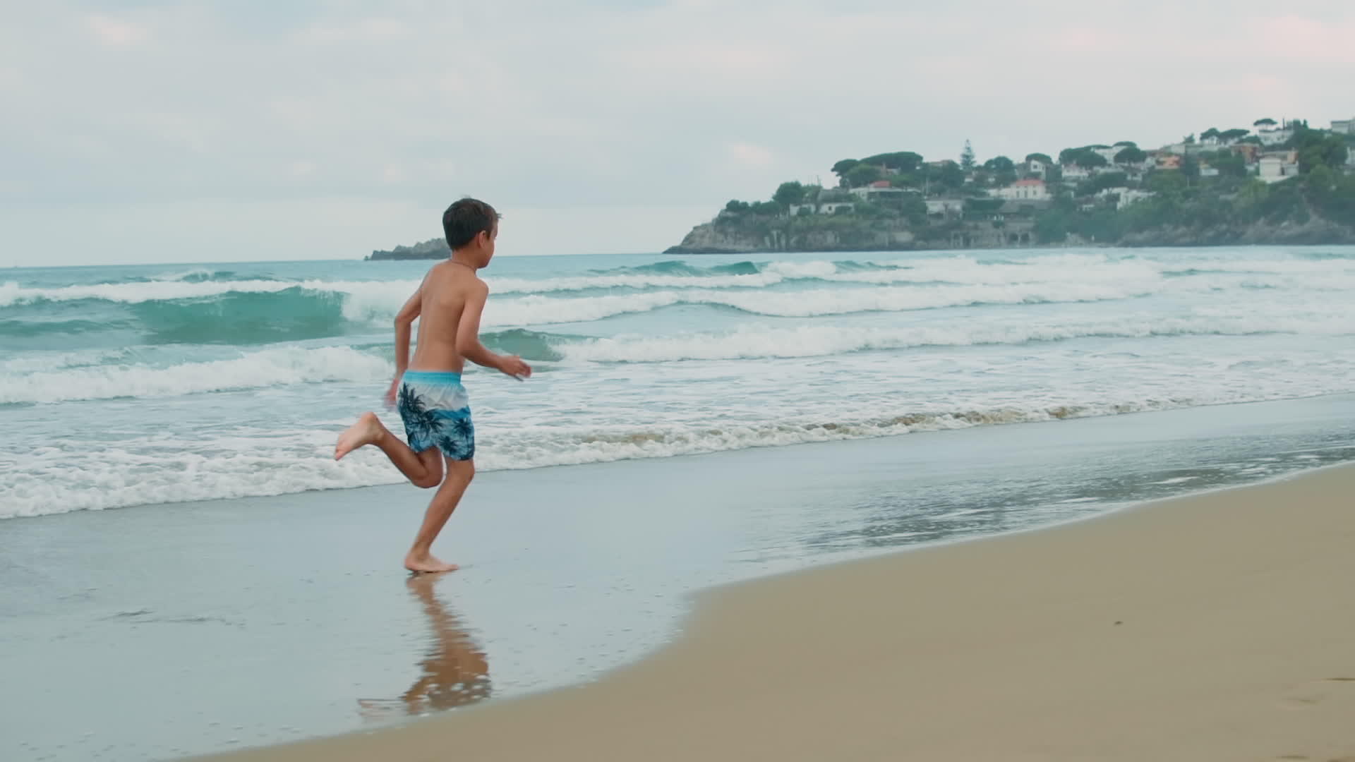 快乐的男孩在海滩上享受暑假沿着海浪奔跑视频的预览图