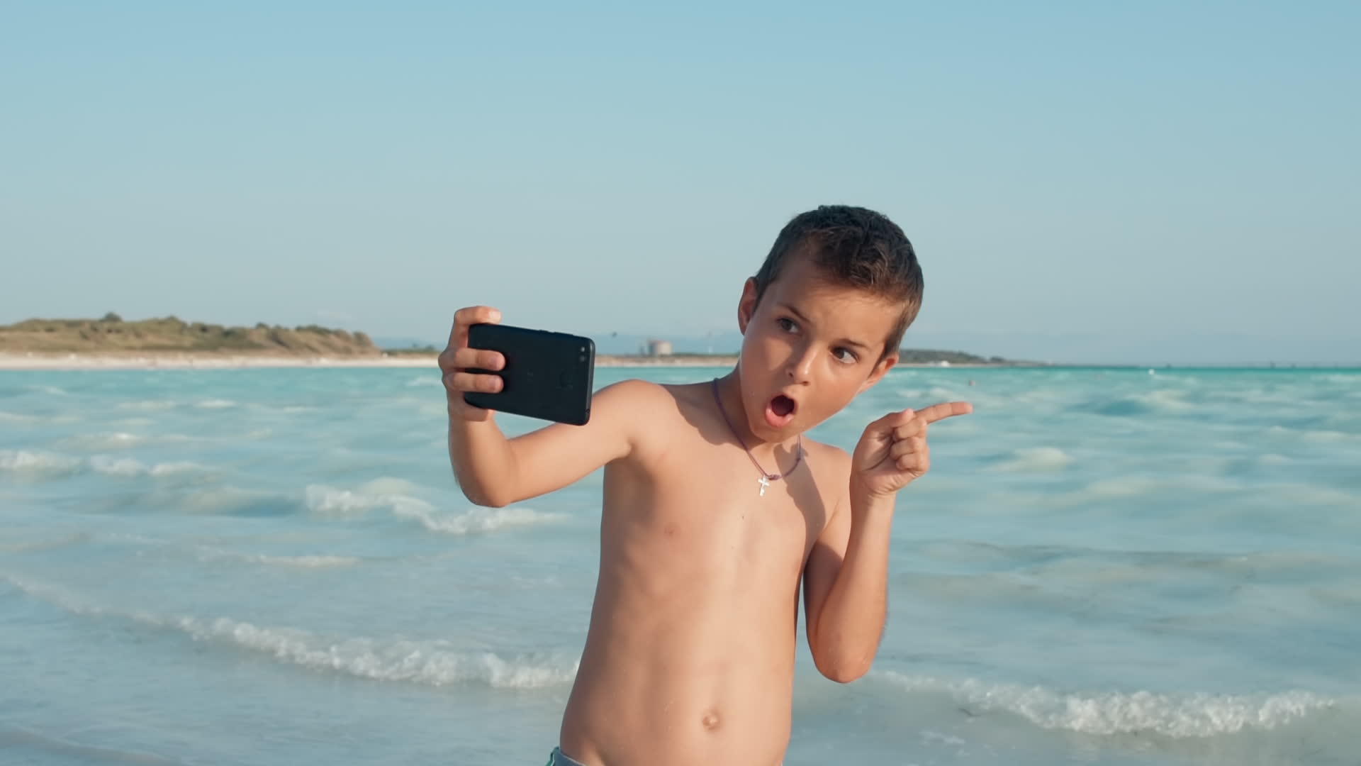 小男孩在海边享受暑假用手机自拍视频的预览图