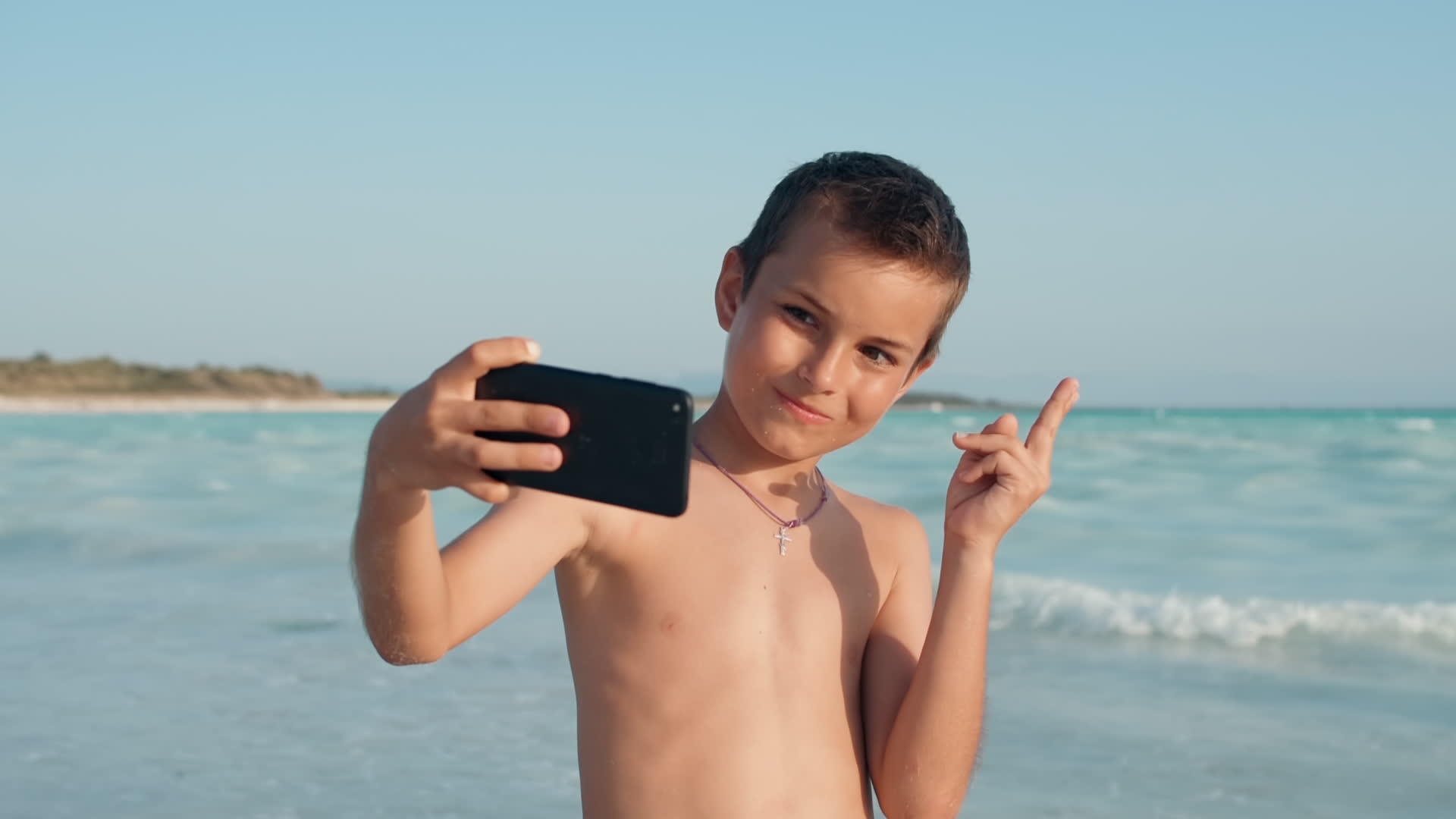 小男孩在海边用手机自拍视频的预览图
