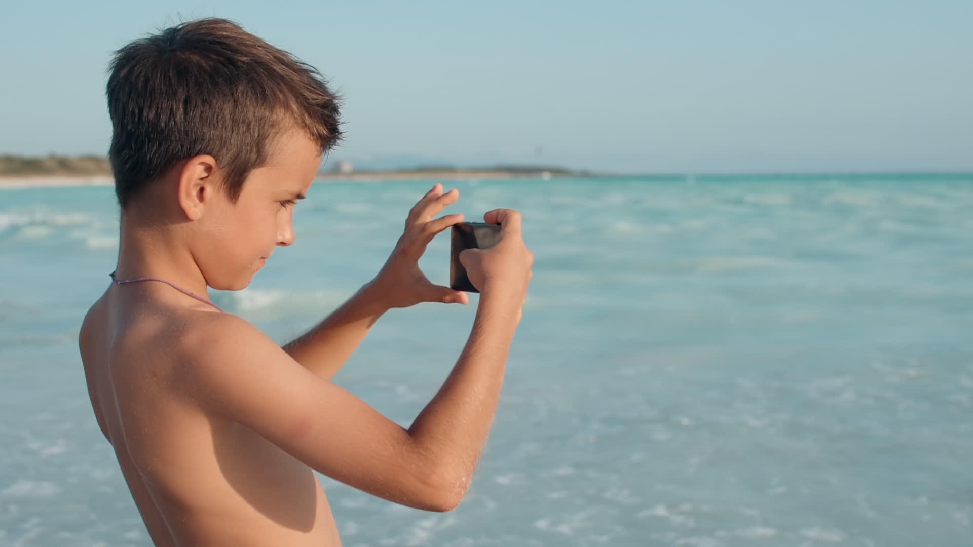 男孩在海边的手机上拍照视频的预览图