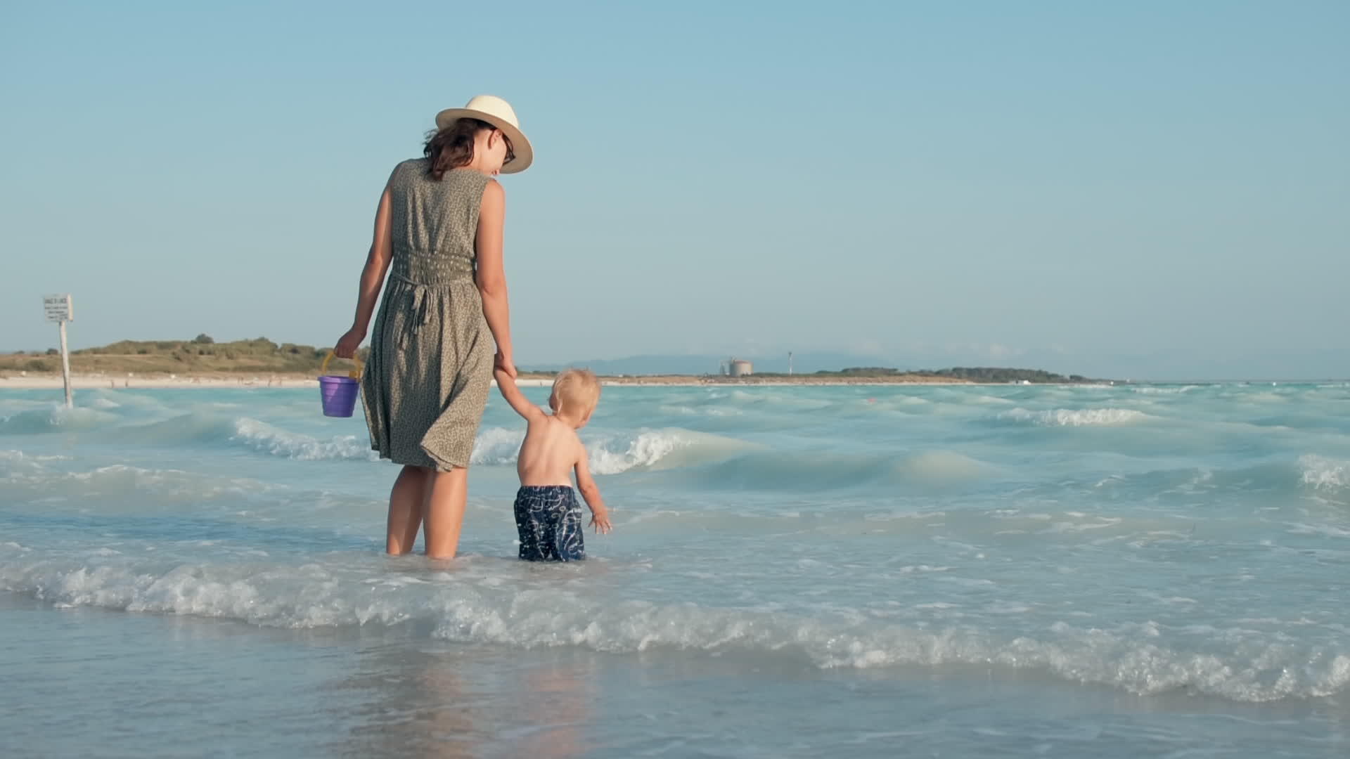 快乐的女人牵着宝宝的手在海浪海滩上行走视频的预览图