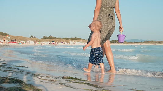 母亲牵着婴儿的手走在海滩上视频的预览图