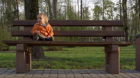 小男孩坐在公园的木凳上视频的预览图