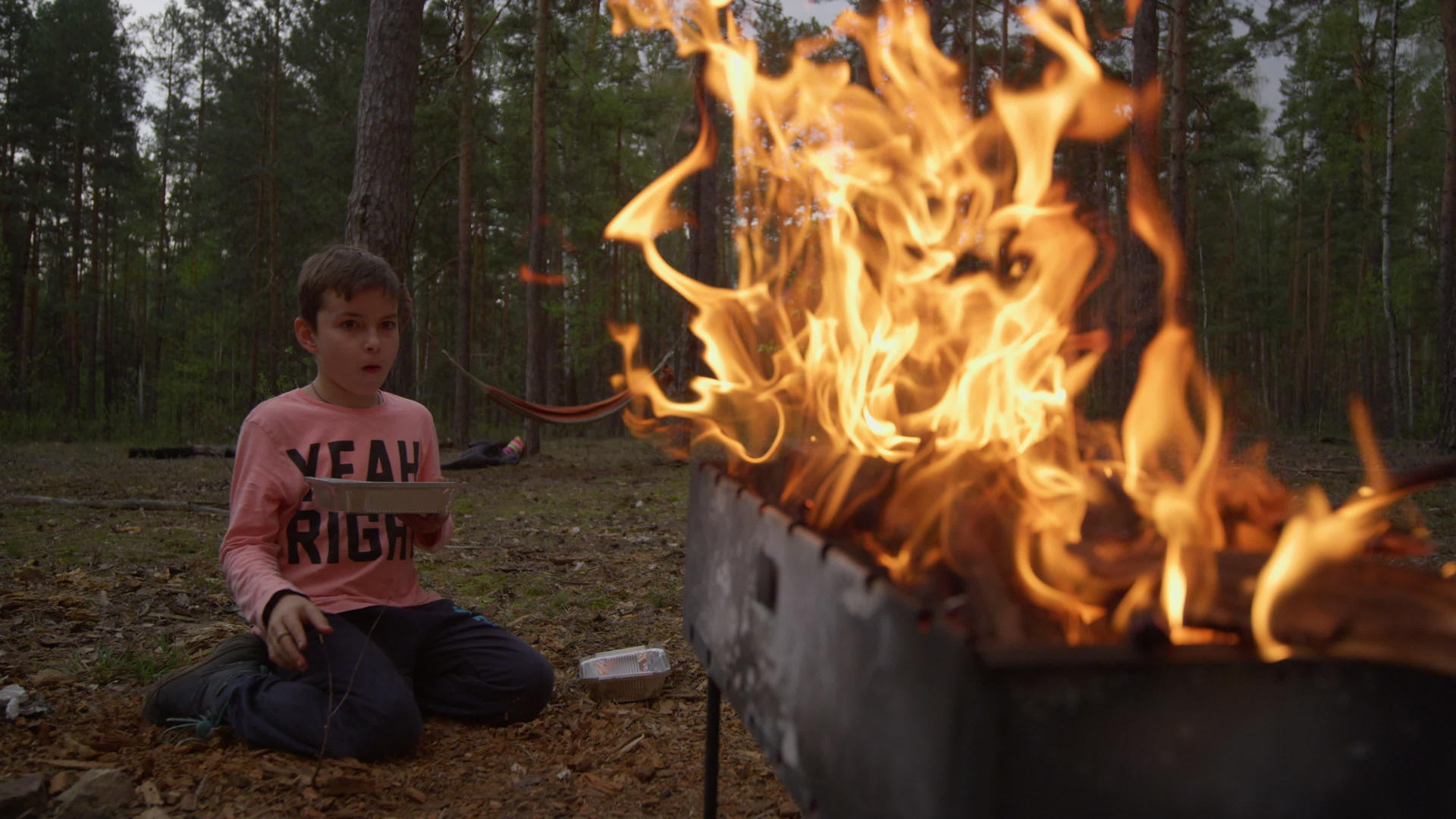 烧烤架上明亮的火焰照亮了男孩坐在炉子旁边的侧影视频的预览图