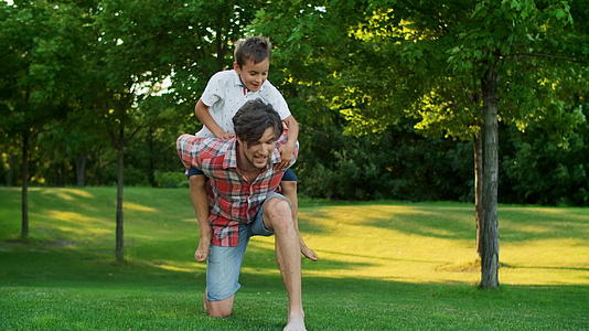 儿子在绿色公园与父亲互动跳到父亲的背上视频的预览图