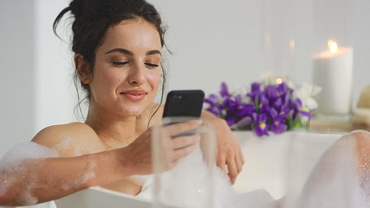 沐浴在浴缸里的女人用智能手机聊天慢动作视频的预览图