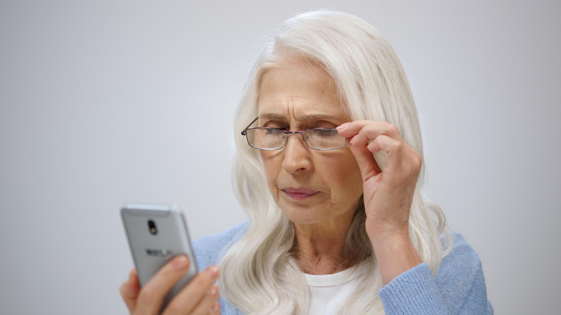 老年妇女用老花镜看着手机屏幕视频的预览图