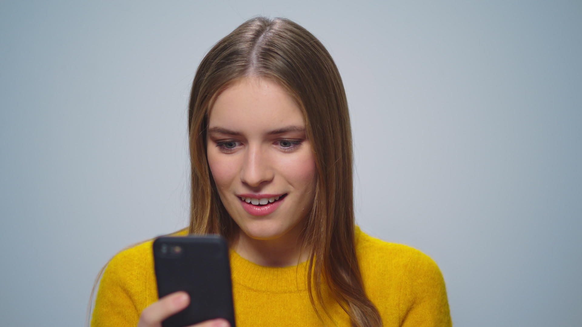 迷人的微笑女性肖像在灰色背景上使用智能手机视频的预览图