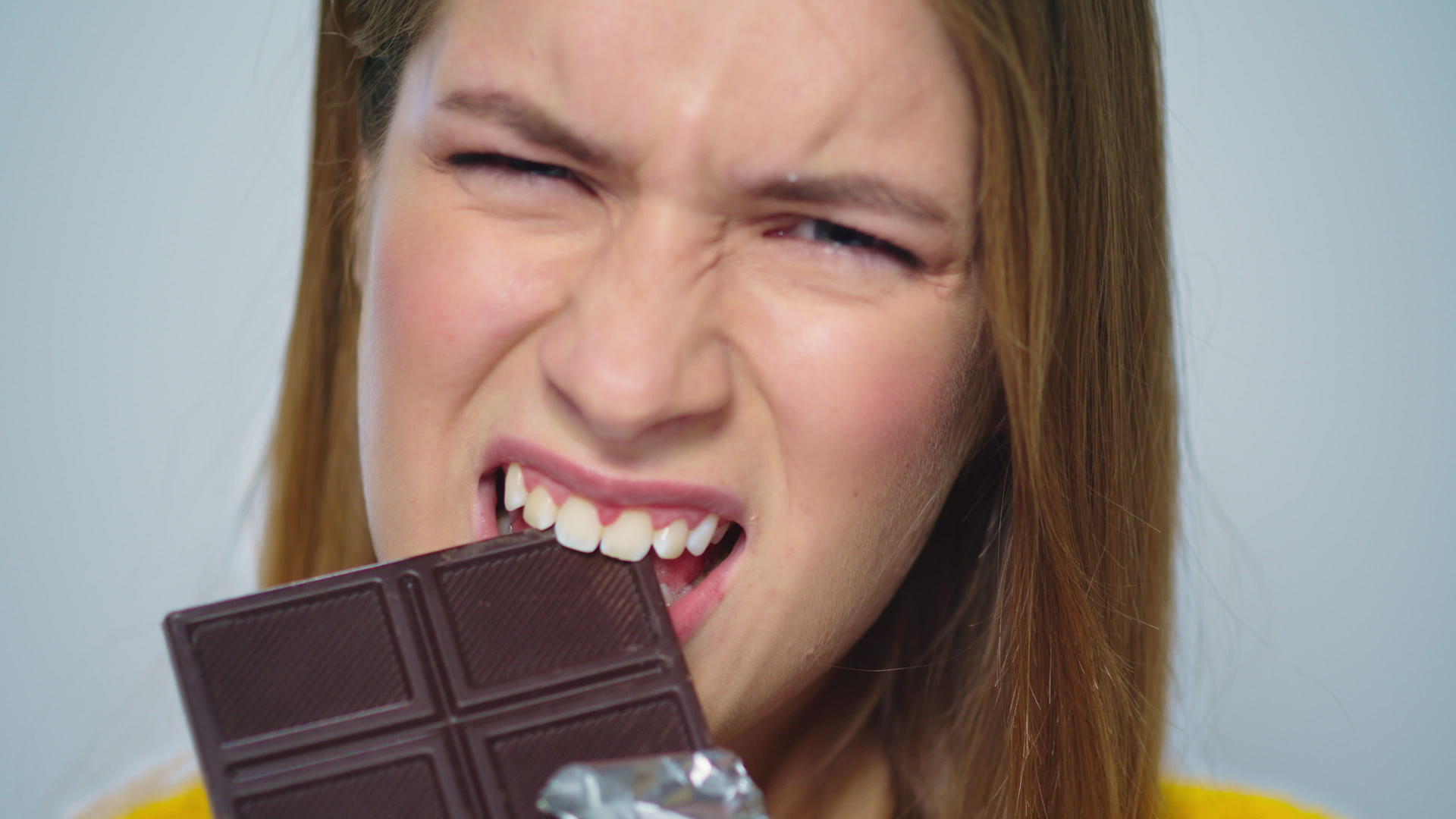 特写欢快的女士在灰色背景的相机上吃巧克力视频的预览图