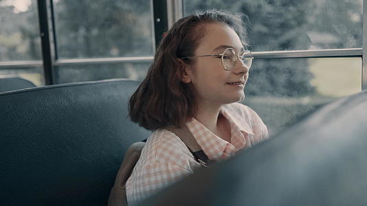 微笑的女学生戴着眼镜坐在公共汽车窗前视频的预览图