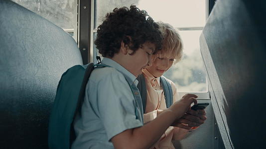 两名学生坐在校车上玩手机游戏视频的预览图