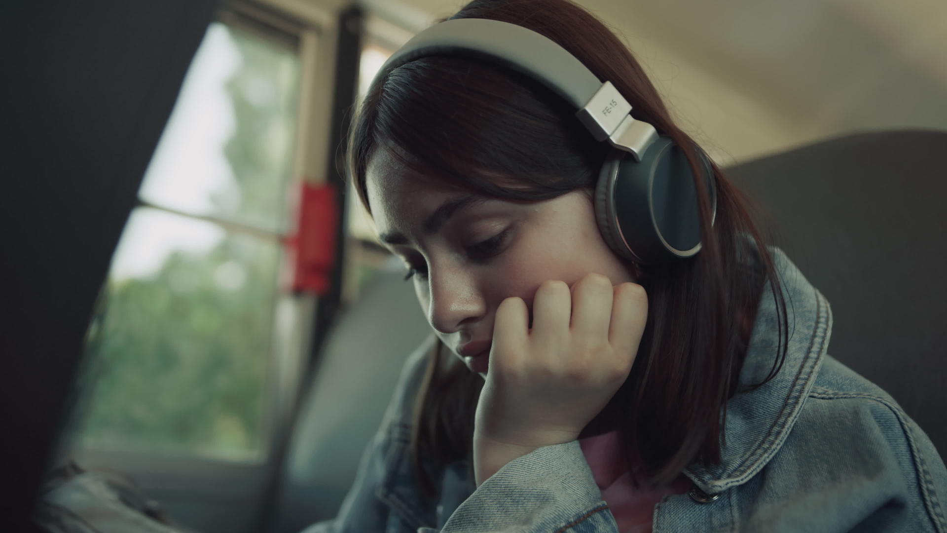 特写让女孩独自坐在校车上戴着耳机等待乘车视频的预览图